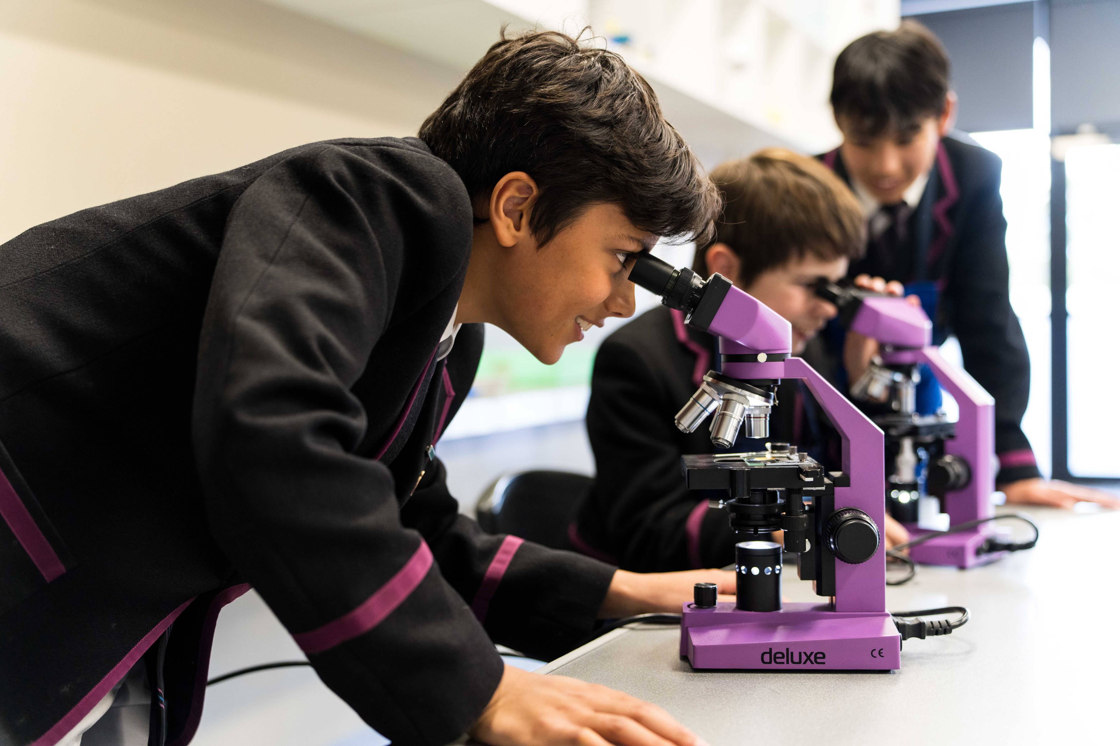 Three Hutchins students in a science class; two are looking through microscopes.